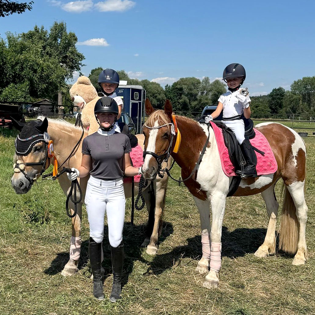 Zwei Mädchen sitzen auf ihren Ponys und winken in die Kamera